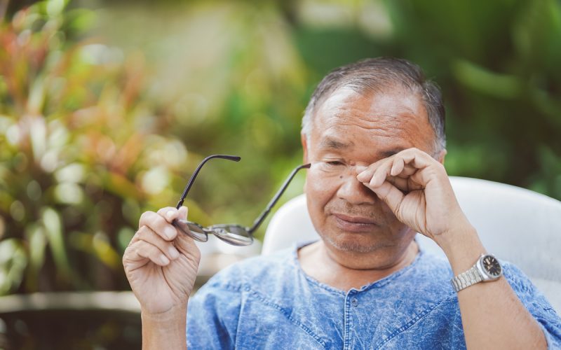 Elderly man rubbing his eyes while holding glasses due to overuse of the eyes, causing itching and irritation.